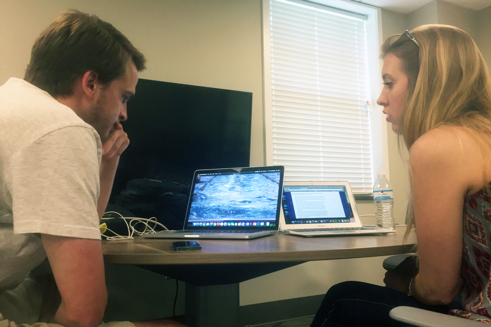 Queens students Austin Huddy and Caroline Henry discuss a multimedia piece on U.S. Olympic swimming coach David Marsh by speakerphone with student Abby Tolar