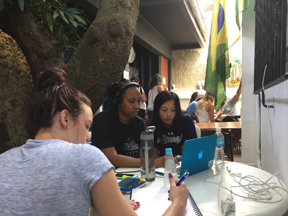 Jamie Doolittle, Tyler Greene, and Becca Chen of the JBT Production team write copy and edit video in their Rio de Janeiro hostel for a multimedia story on Sugarloaf Mountain. The team is covering the impact of the Rio 2016 Olympic Games on the city.